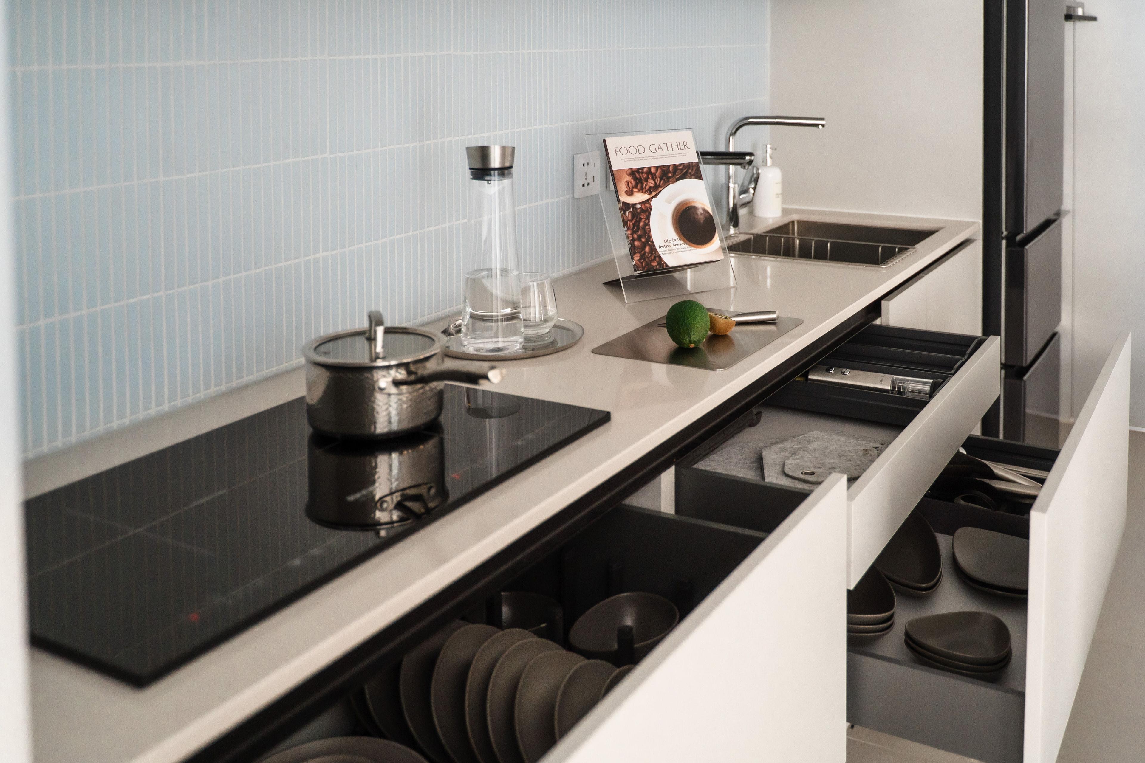 Moderne Küche mit integriertem Kochfeld, offenem Geschirrschrank und Spüle auf einer weißen Arbeitsplatte vor hellblauer Fliesenwand.
